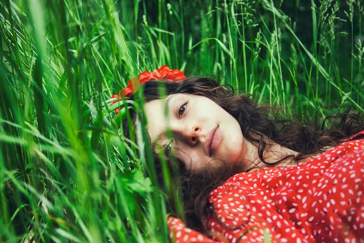 Beautiful girl in a red dress and with a flower crown resting in the grass