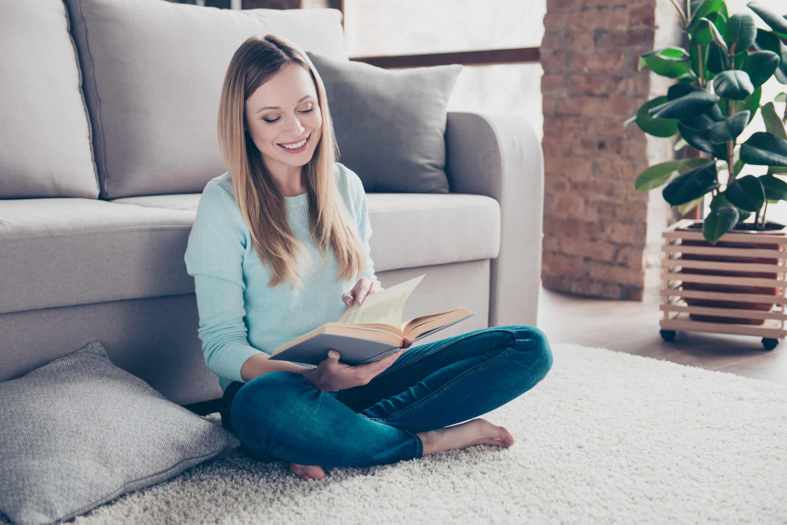 Woman reading a book while sitting comfortably on the floor in living room.
