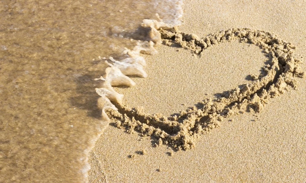 Heart drawn on sand is washed off by sea wave.