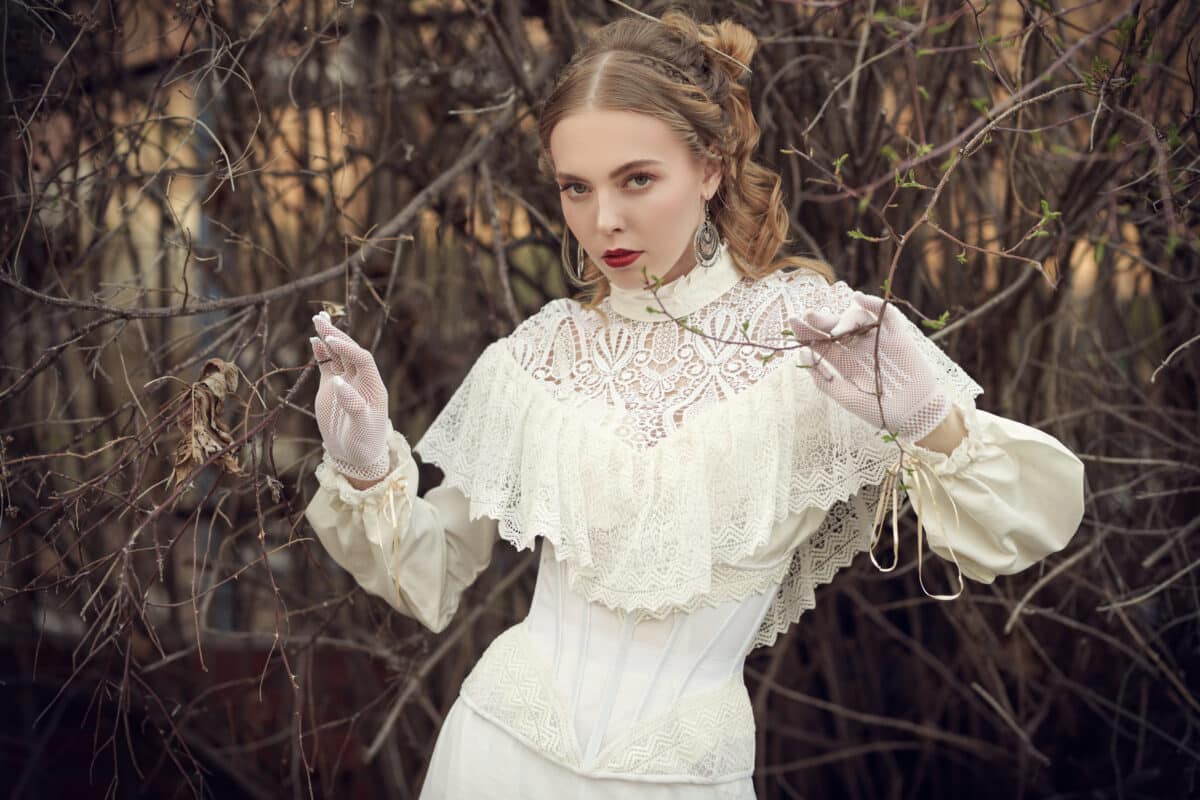 a beautiful noble lady from victorian era wears a white lace dress stands in a spring park among the bare branches of trees