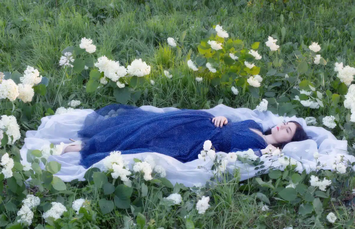 young beautiful woman in blue dress on grass with white flowers