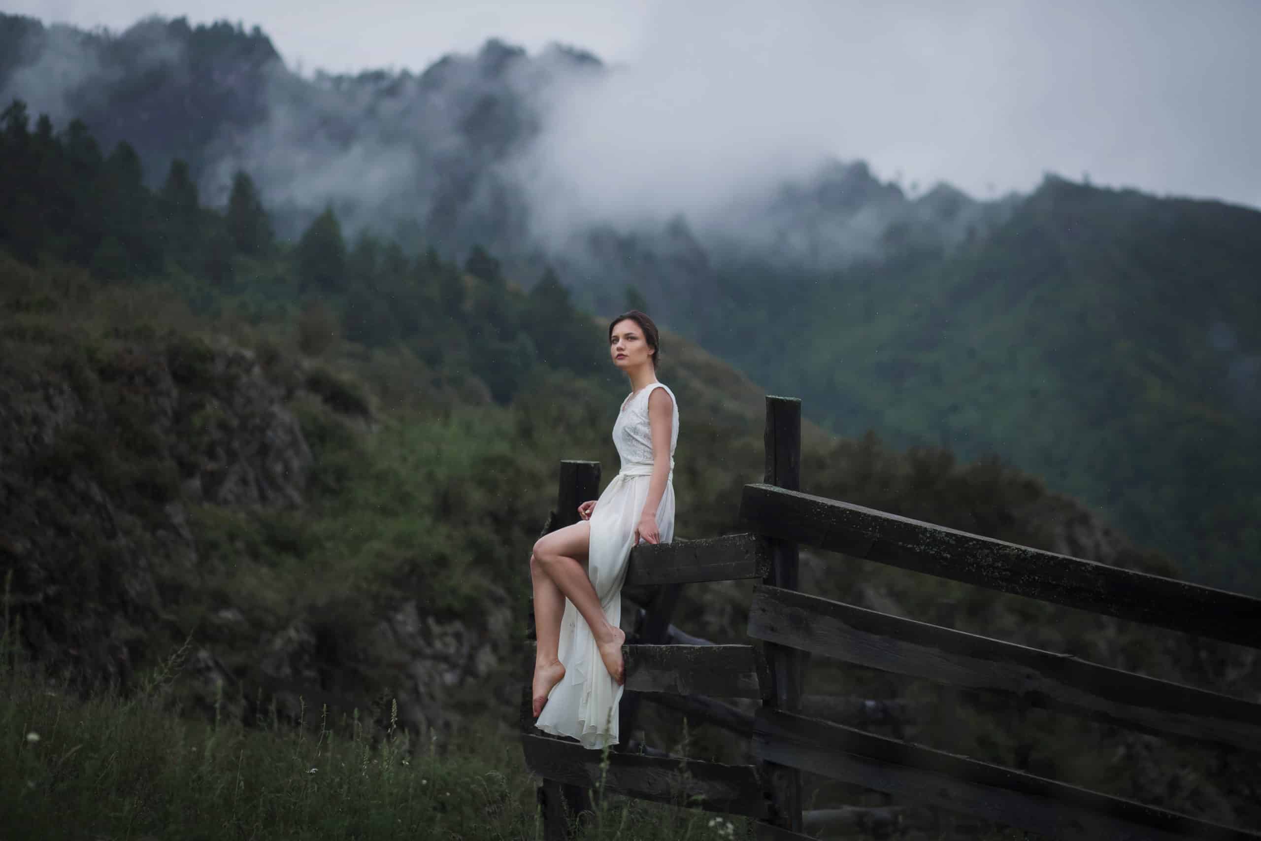 Lady in white sitting on a fence, fog in the background.