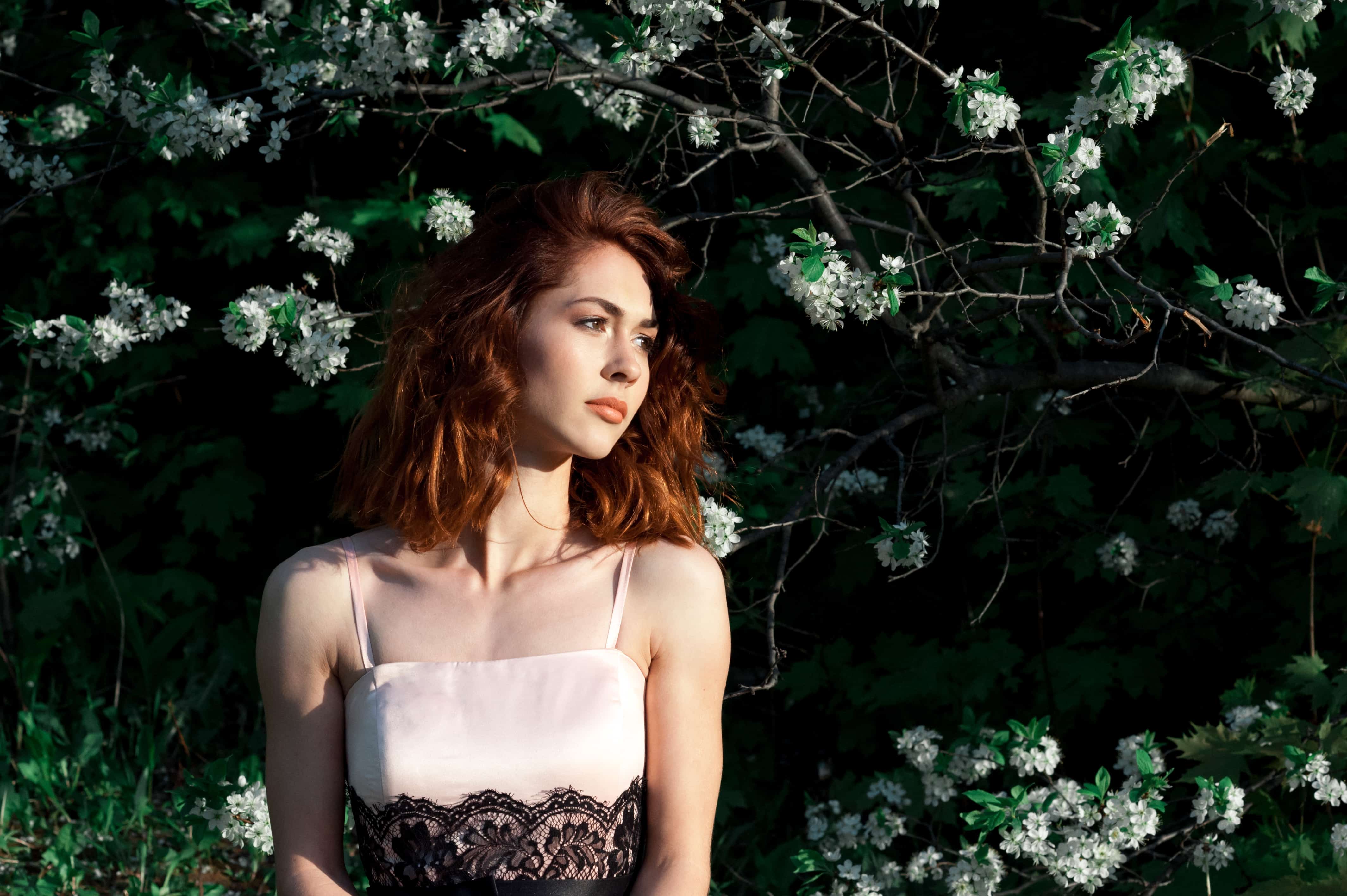 young lady with gorgeous dark red hair standing next to the apple trees in bloom