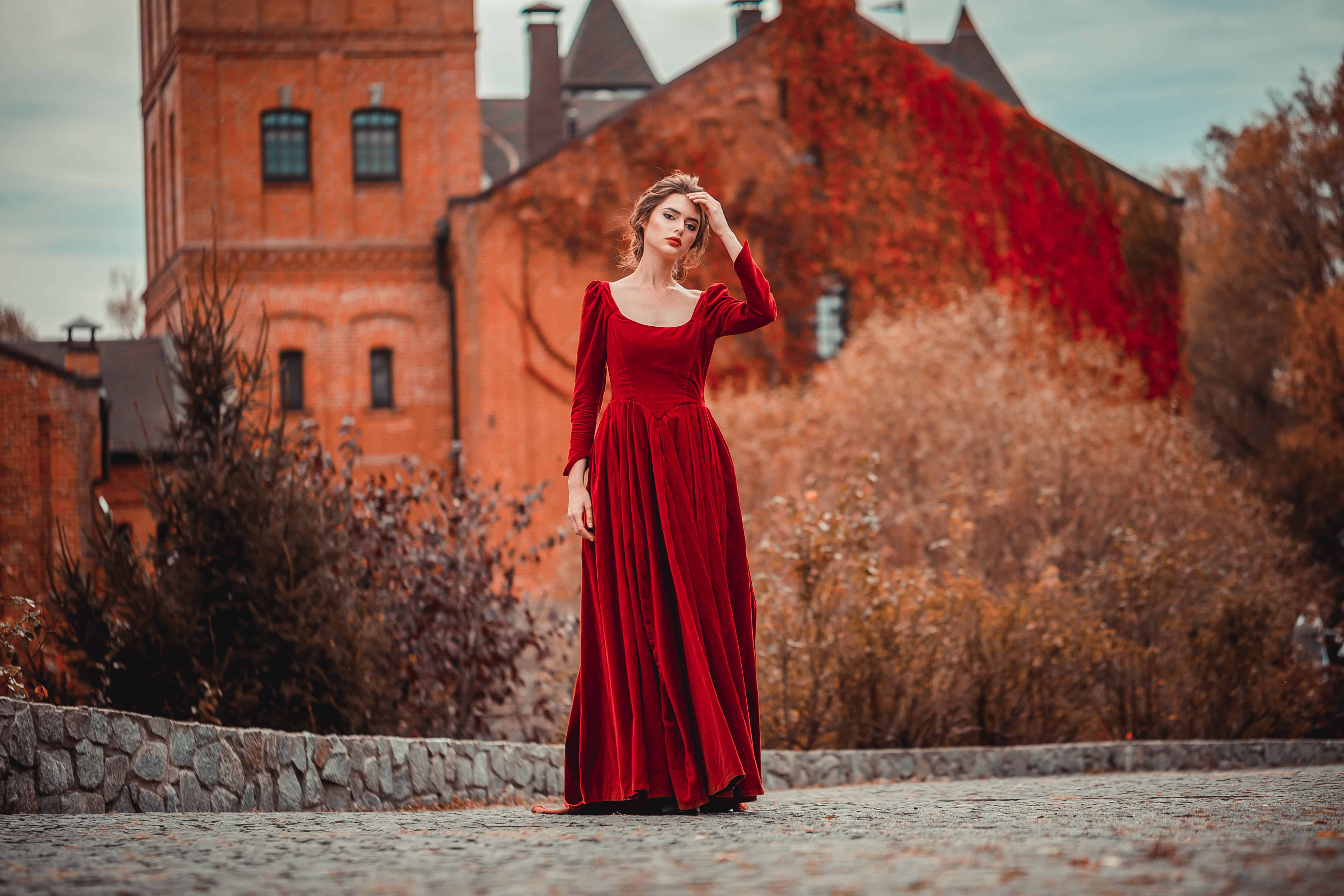 pretty lady in a burgundy red dress walking near an old castle