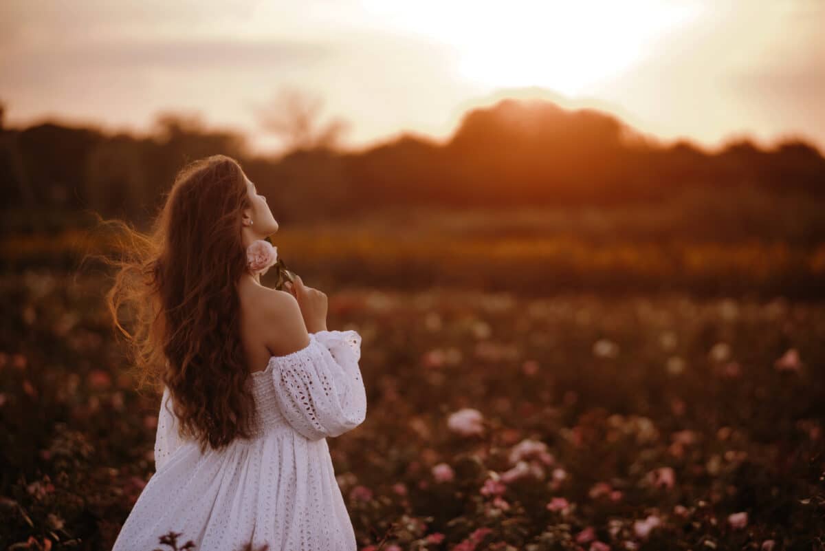 a lady dressed in white holding a rose in the field at sunset