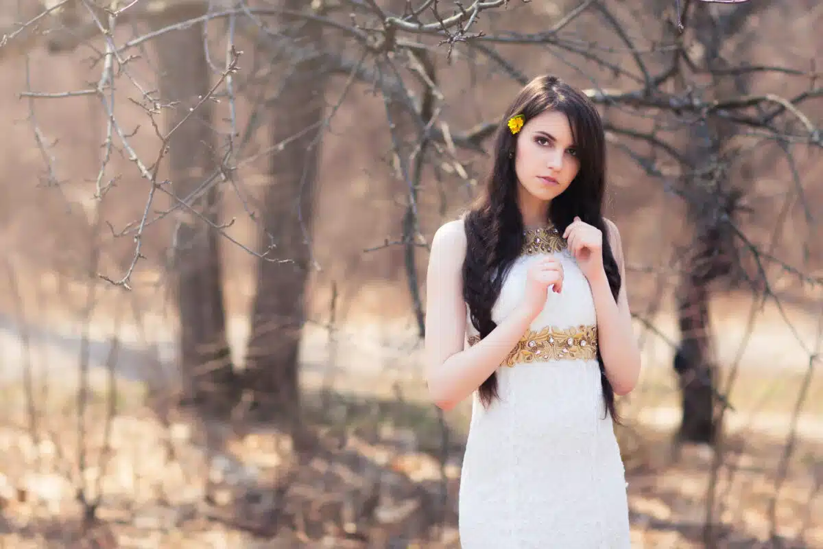 Young beautiful woman with flowers in hair. Braided bride at forest in white dress on blurred autumn background during a wedding photo shoot.