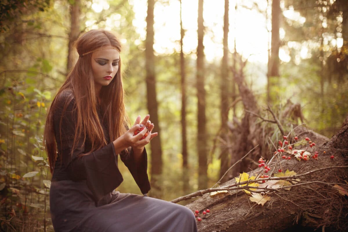 beautiful woman in autumn forest looking at the berries in her hand