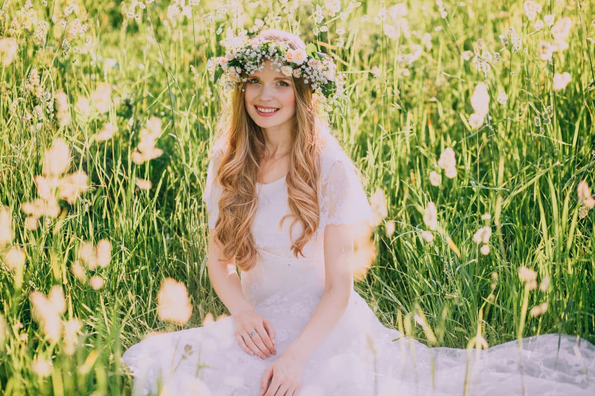 Beautiful young woman with wreath of wildflowers in her hair sitting on the meadow