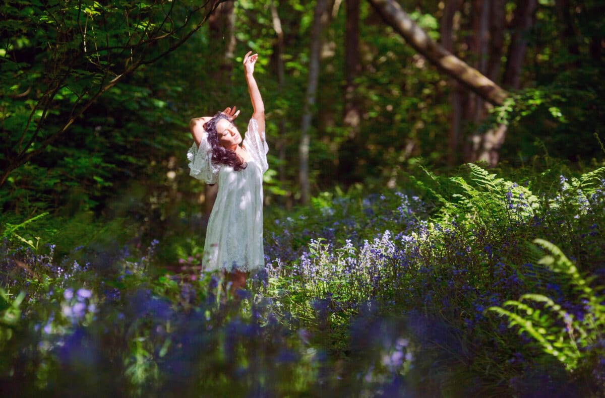 a lady in a white dress walking through a blue bell wood
