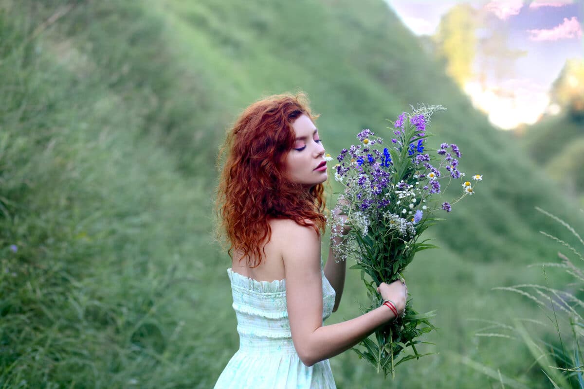 a beautiful young lady in a light summer sundress holds a bouquet of colorful wild flowers