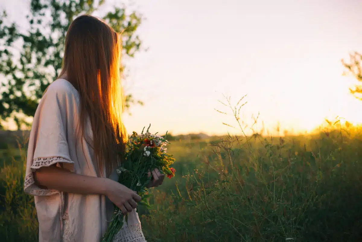 red haired woman holding a bouquet of wild flowers in nature at sunset