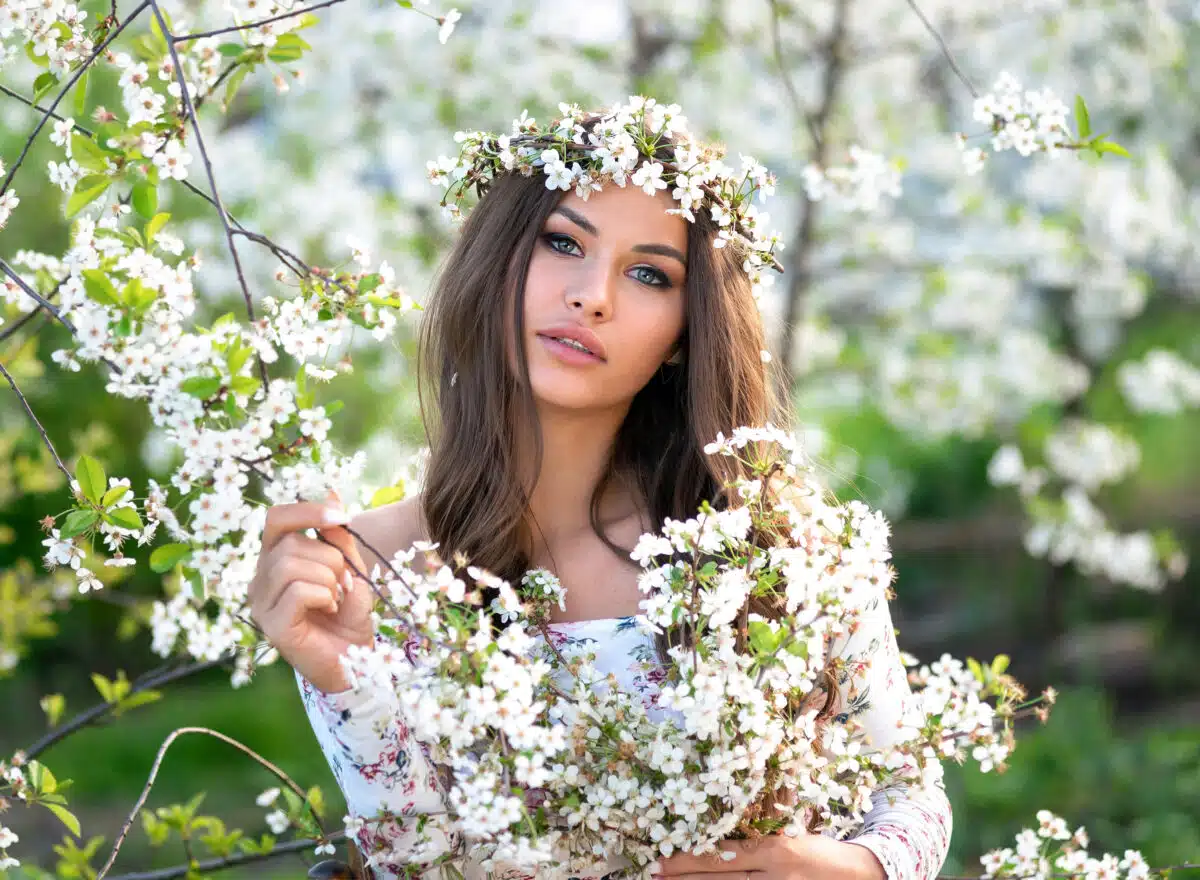 Natural beauty with wreath on her head and bouquet of cherry branches in the summer garden, enjoying the blooming spring nature