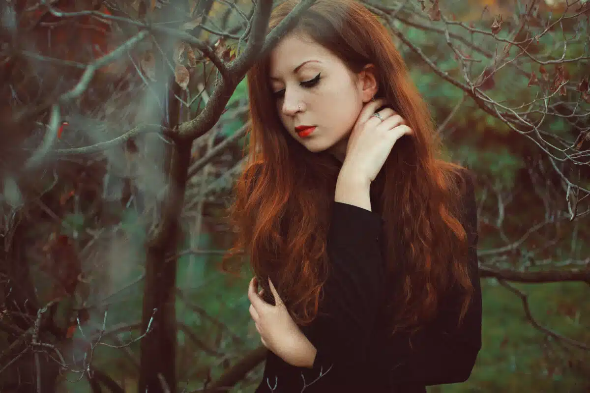 a pretty but melancholic redhead woman in the forest