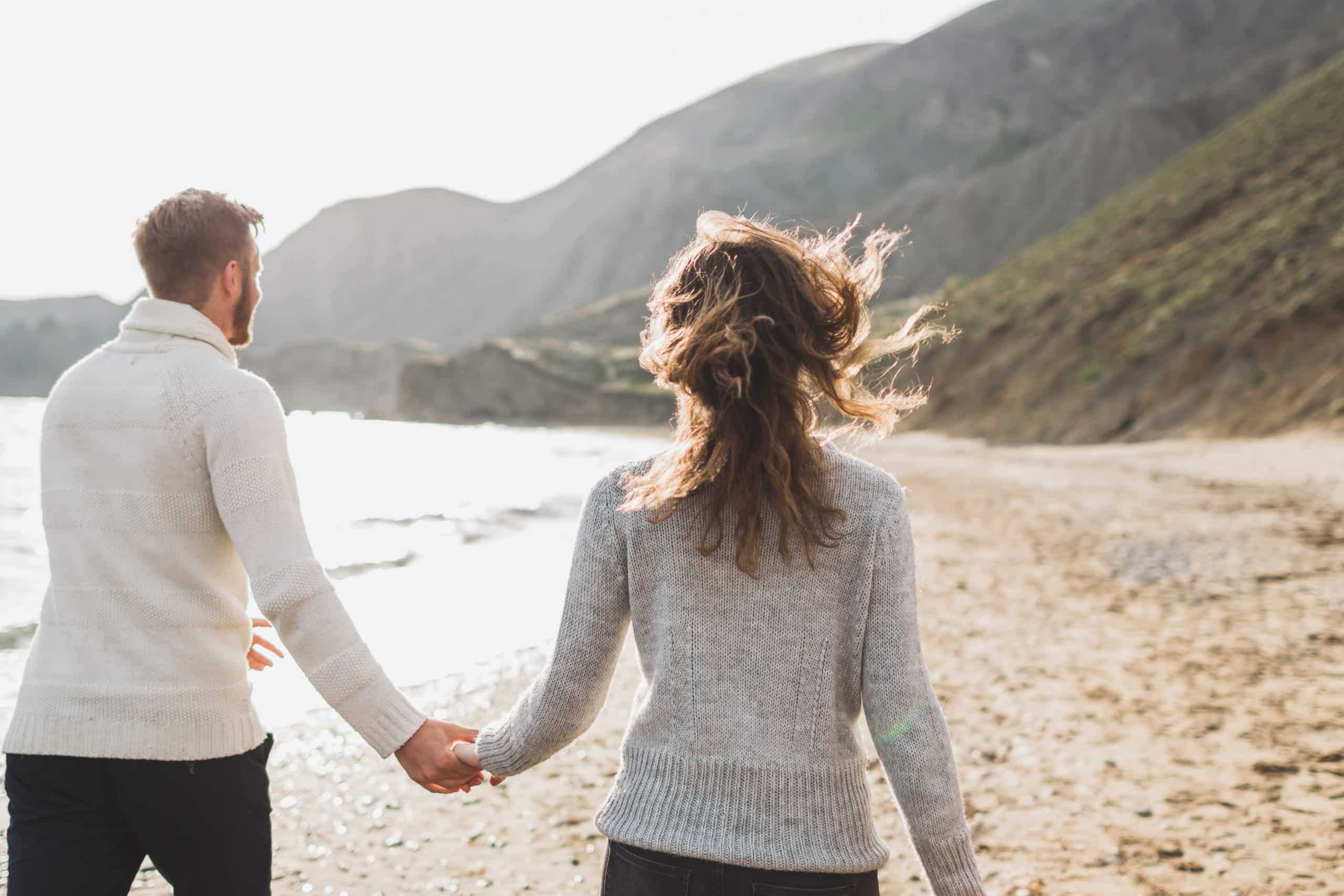 Man and woman in love holding hands as they walk on a breezy beach.
