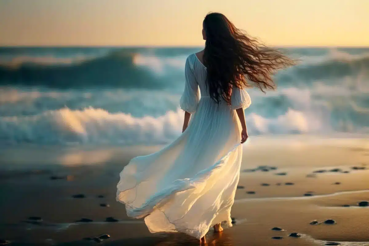 a beautiful lady with long flowing brown hair in white fluttering dress in the wind against the background of the sea at sunset