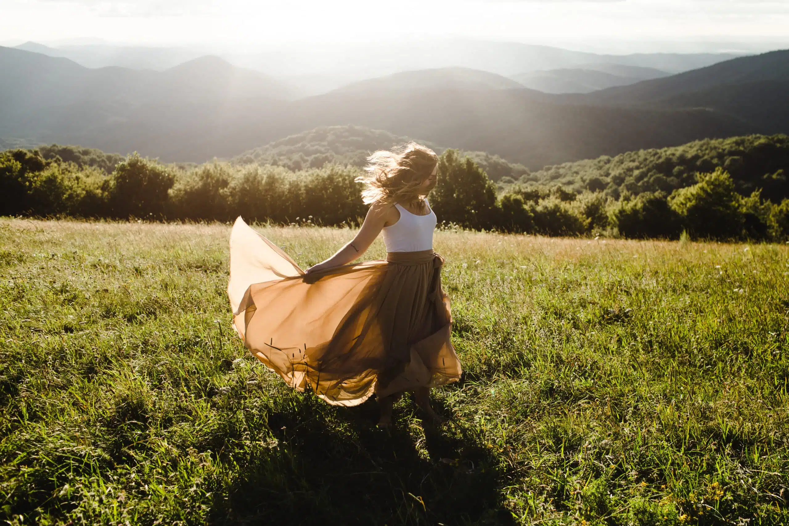 Woman with long dress running in a meadow in the mountains