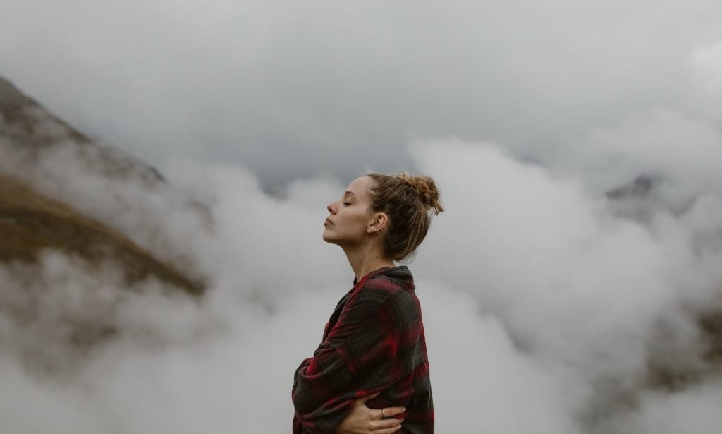Woman standing on a misty mountain, looking sad and pensive.