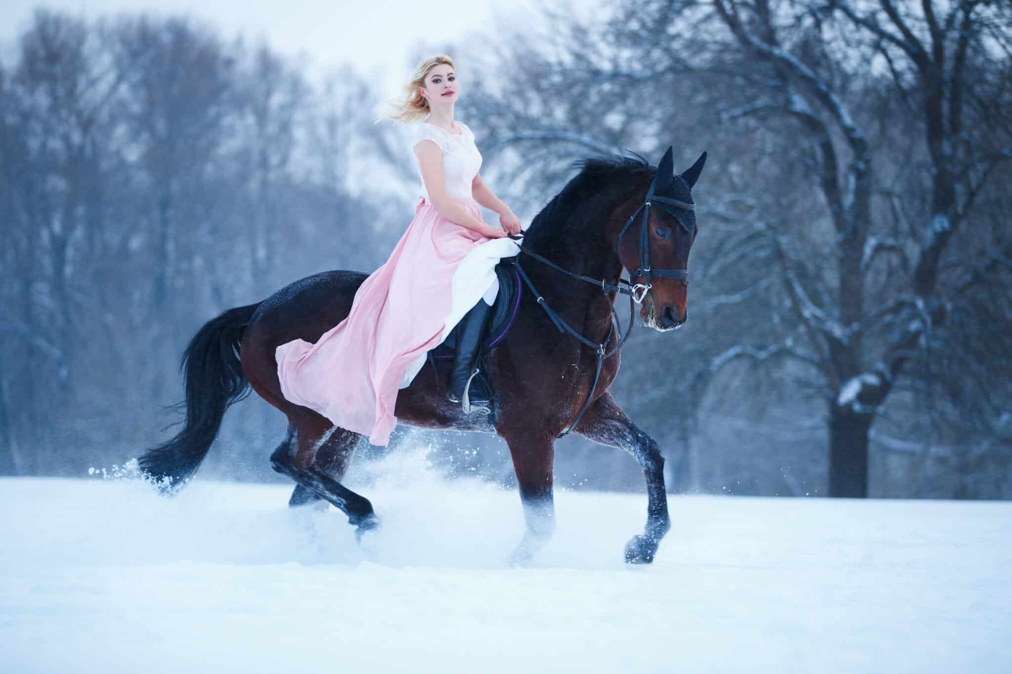 Young woman in dress riding a black horse on winter field