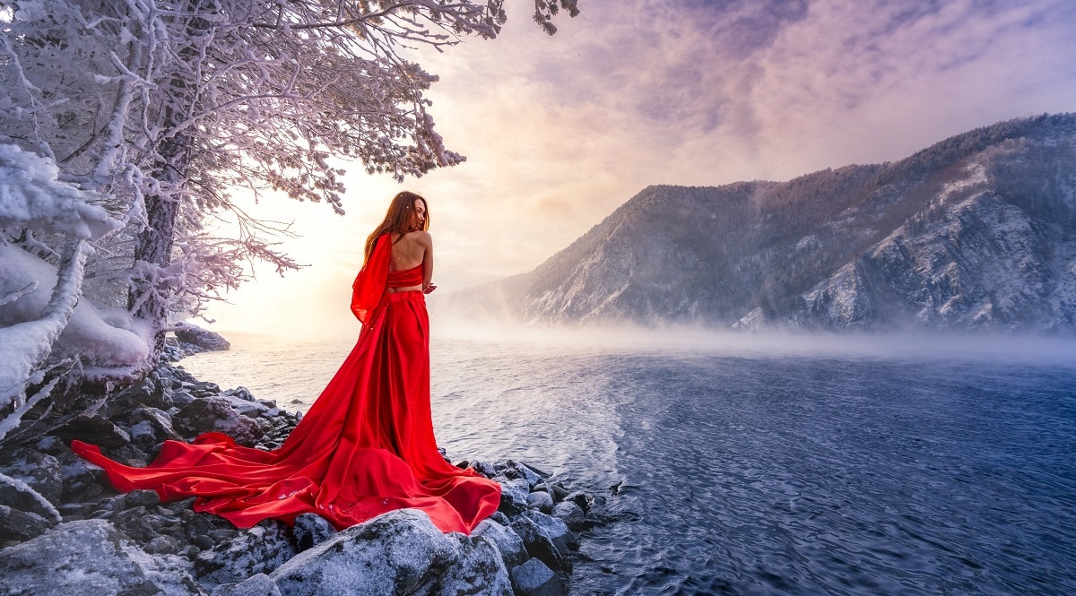 lady in a red dress standing on the shore of a misty lake
