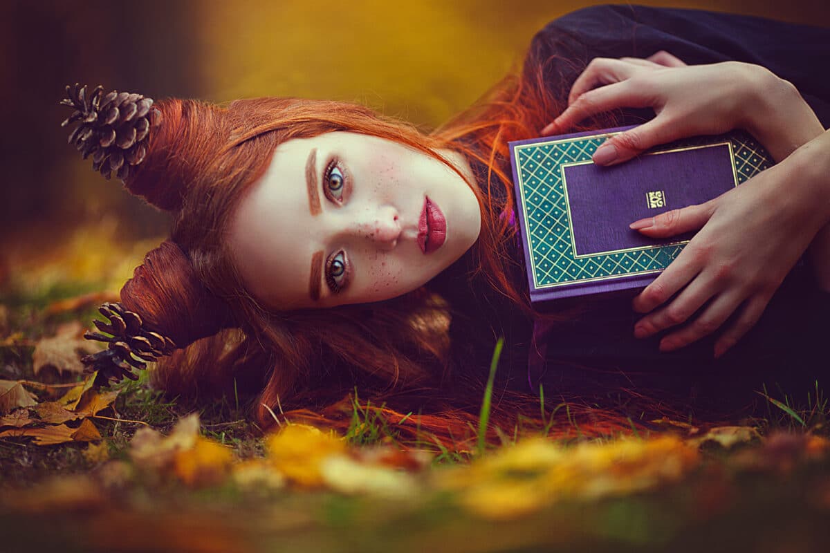 Portrait of a beautiful red-haired girl with an unusual hairdo with a book in the autumn fairy forest. A fabulous autumn photo shoot.