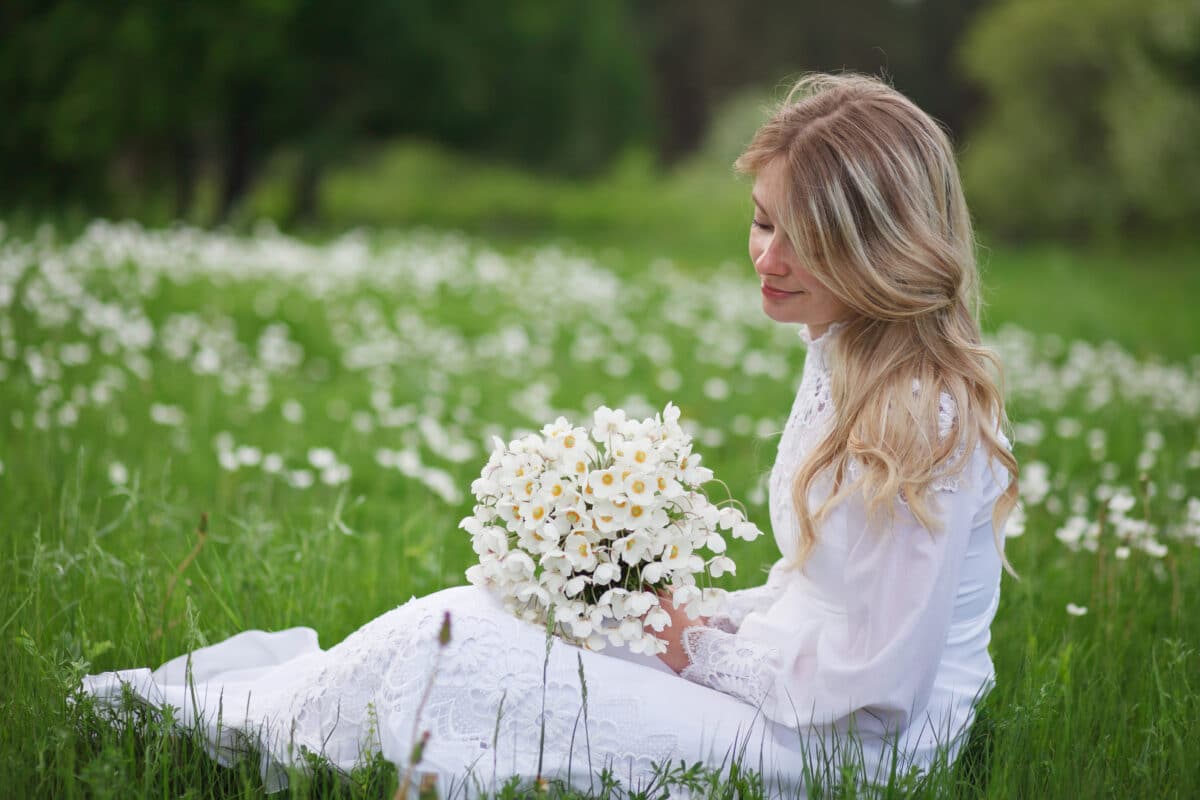 
beautiful blonde in a vintage white dress walks in a blooming apple orchard