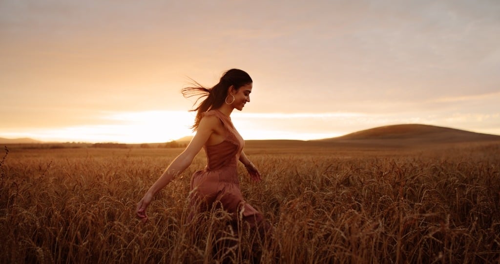 Young happy woman walking in a field at sunset.