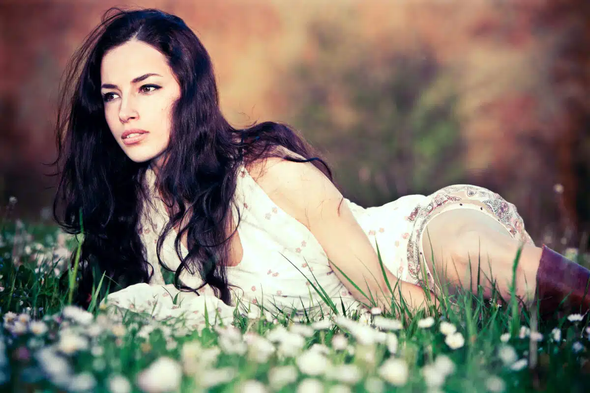 enchanting woman with long black hair relaxing on the grass with white flowers