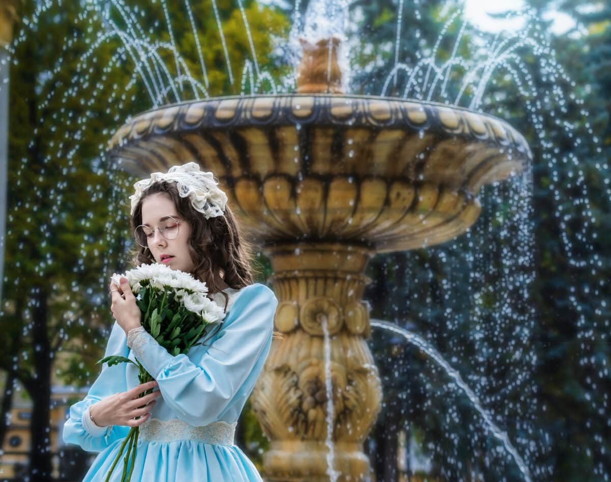 Portrait woman with a bouquet in vintage dress standing by fountain