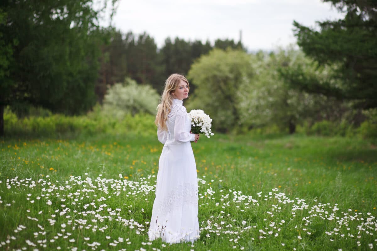 a beautiful blonde in a vintage white dress walks in a blooming garden with anemones