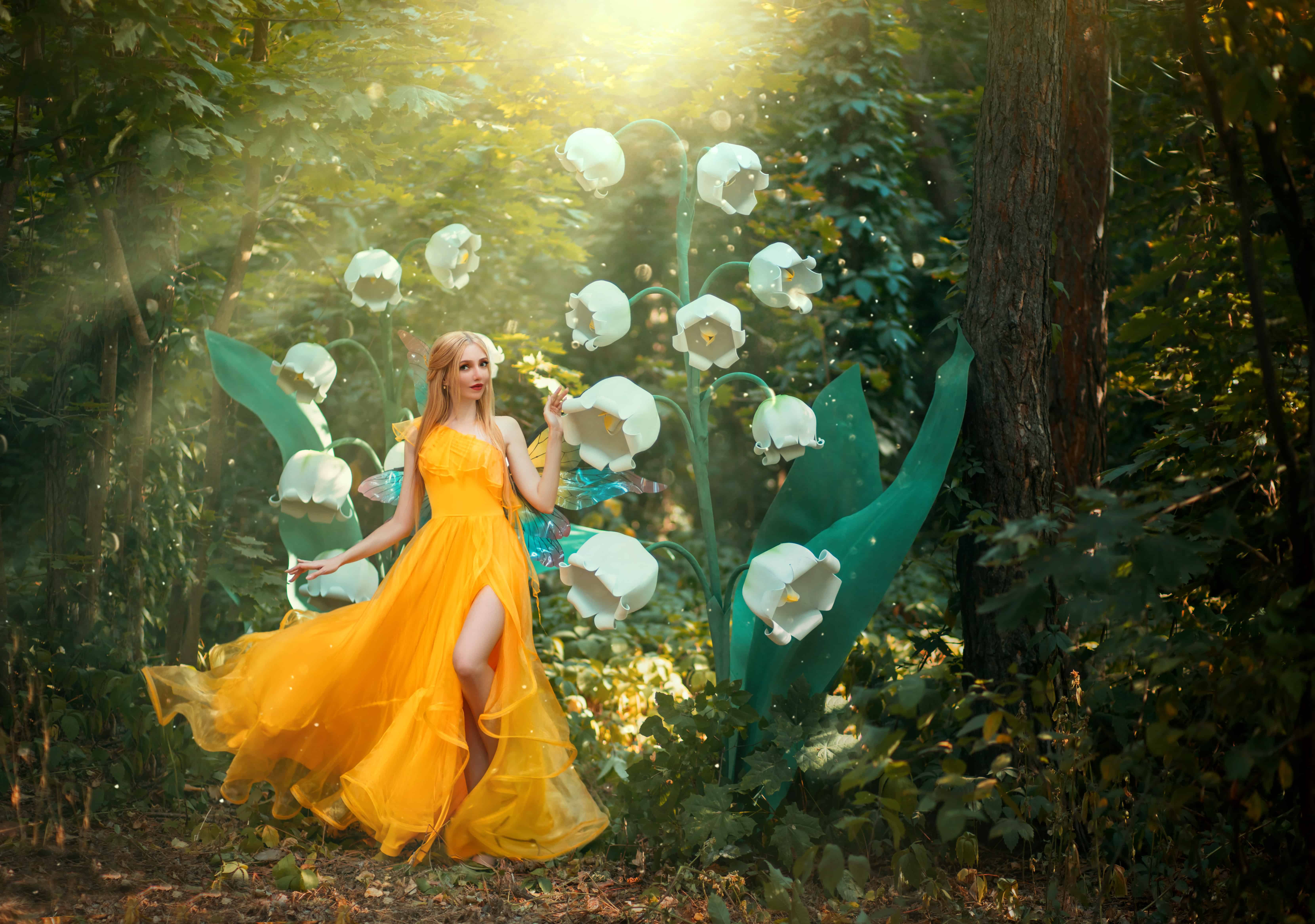 fantasy woman fairy Girl Fashion model walks in spring summer nature deep forest. Large flower white lily of valley. Green tree rainforest Divine magic sun light. Yellow dress silk fabric fly in wind