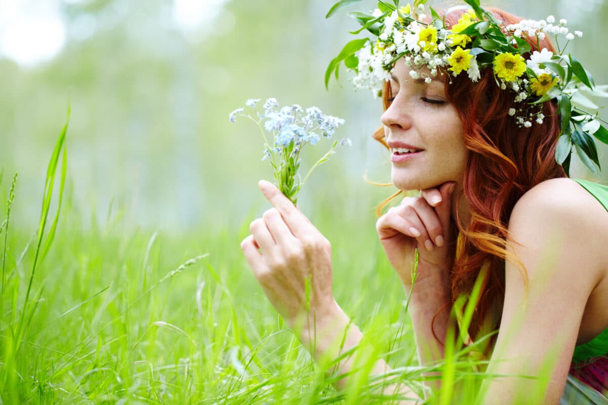 in summer a young lady relaxes on the grass holding and wearing a wreath of wild flowers