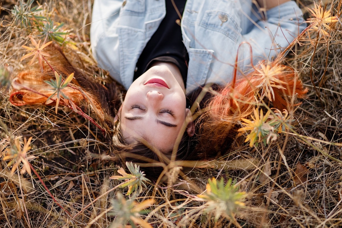 beautiful redhead woman lies in yellow grass with wildflowers in autumn