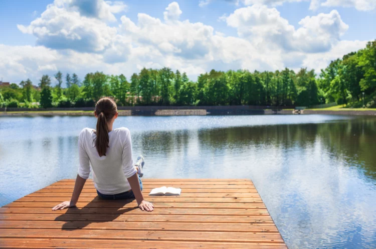 Woman relaxing by a beautiful lake, a notebook beside her.