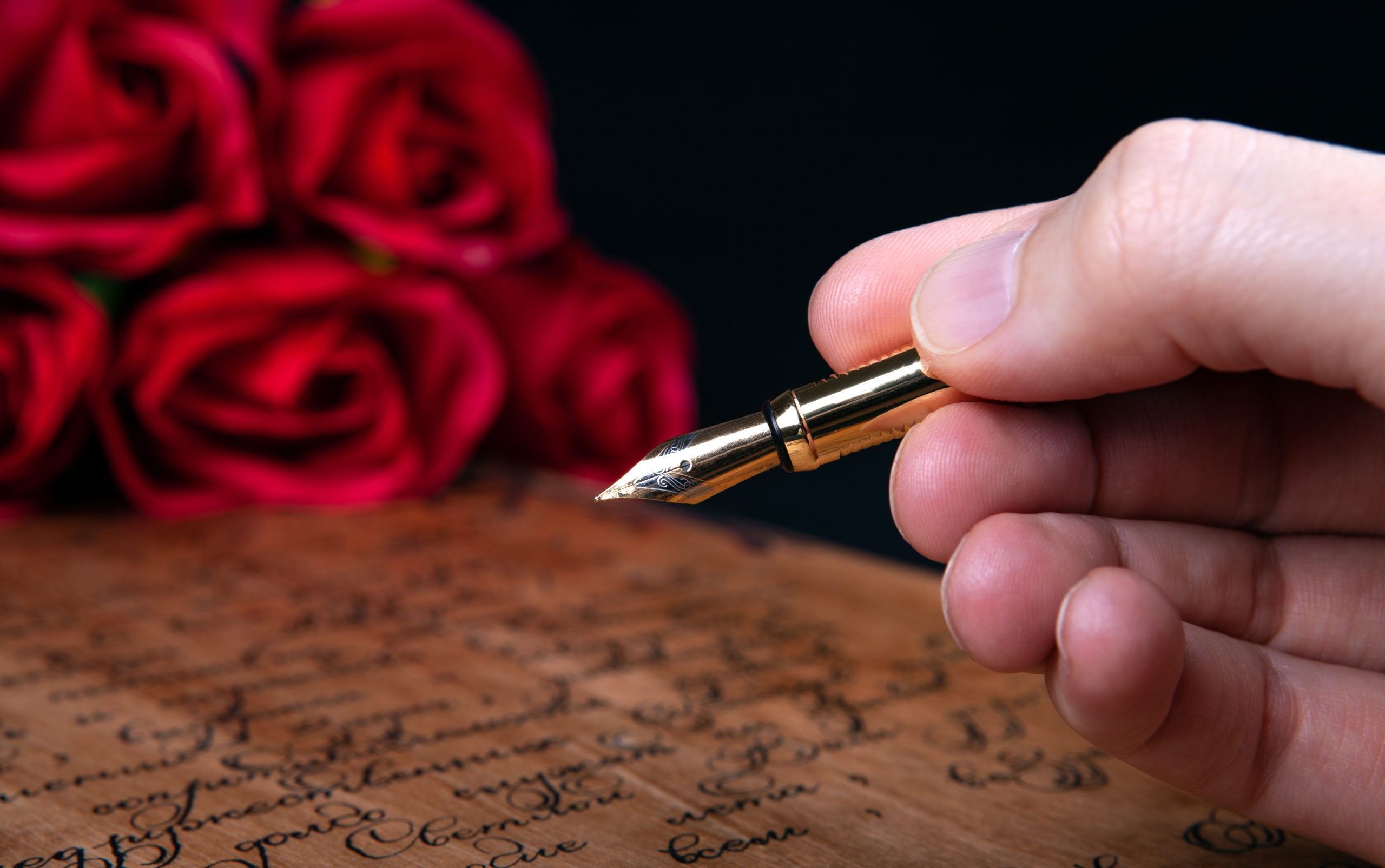 fountain pen in the hand on letter with text and red roses.