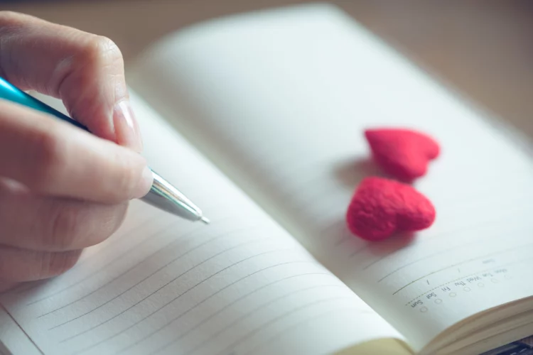 Female hands writing in open  notebook with couple little red hearts