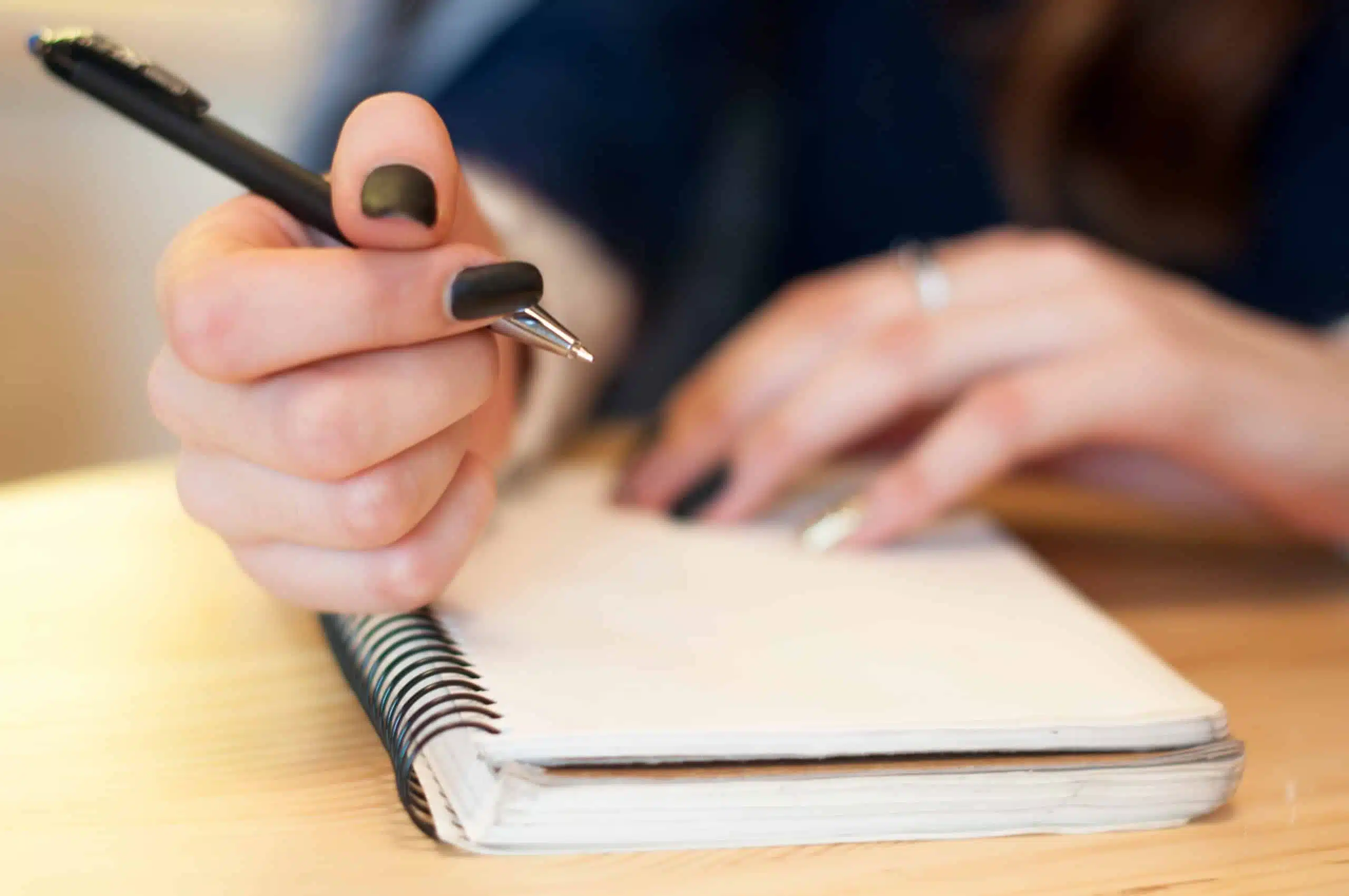 Female manicured hand writing on blank notebook.