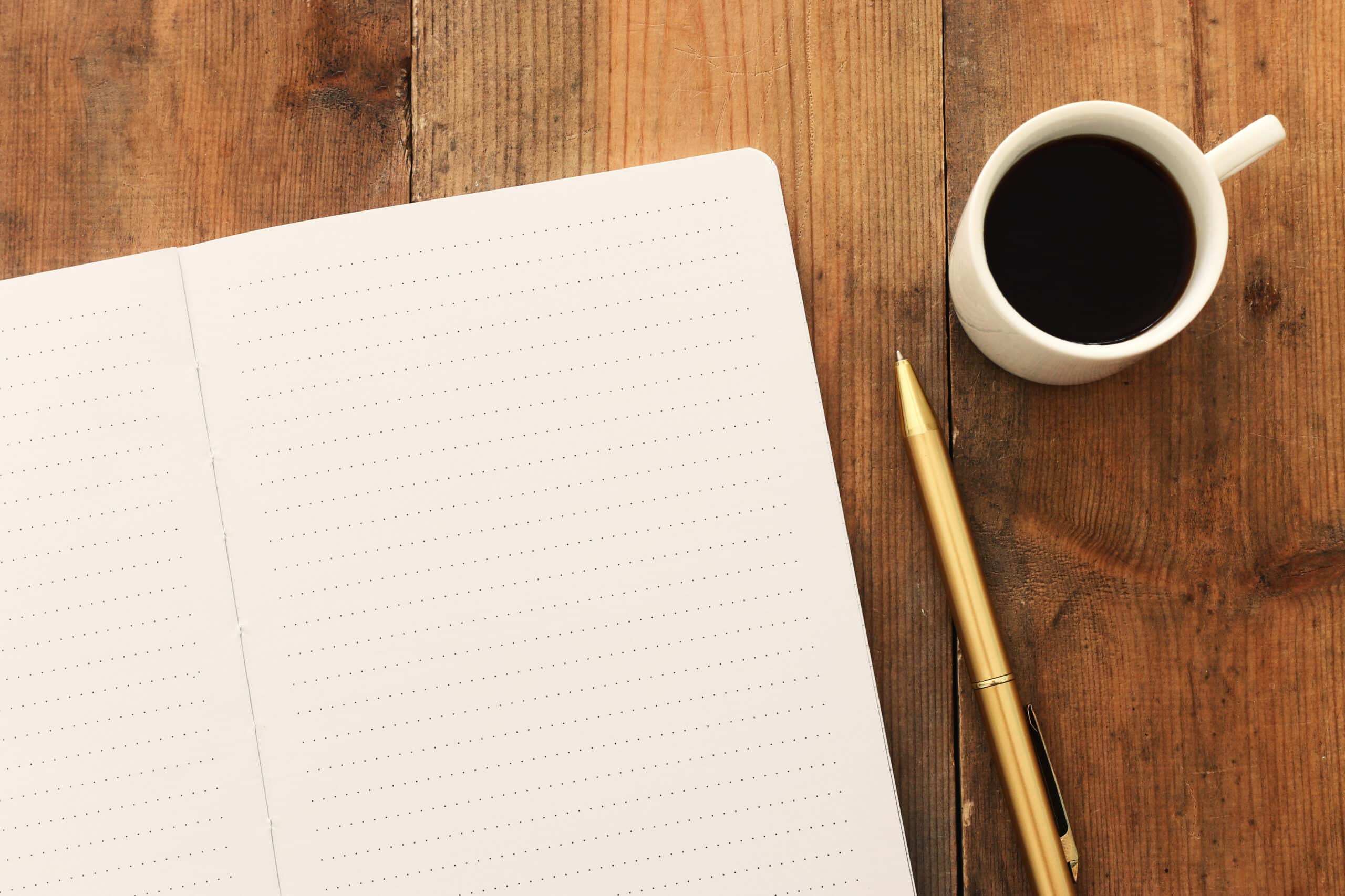 open notebook with blank pages next to cup of coffee on wooden table.