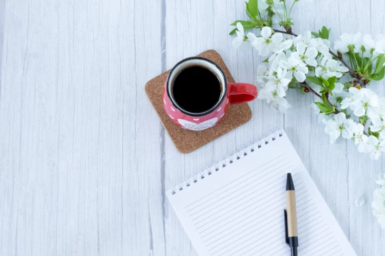 Cup of coffee and a blank notebook on a table with spring flower