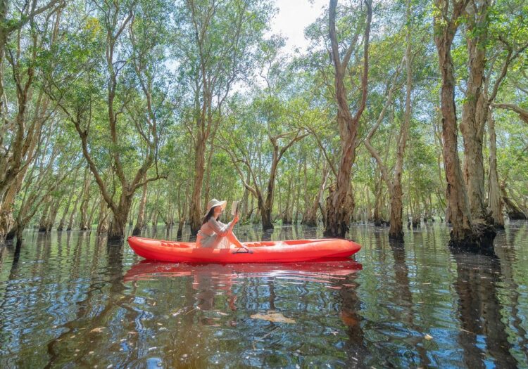 Woman reading a book in a red kayak on the forest river.