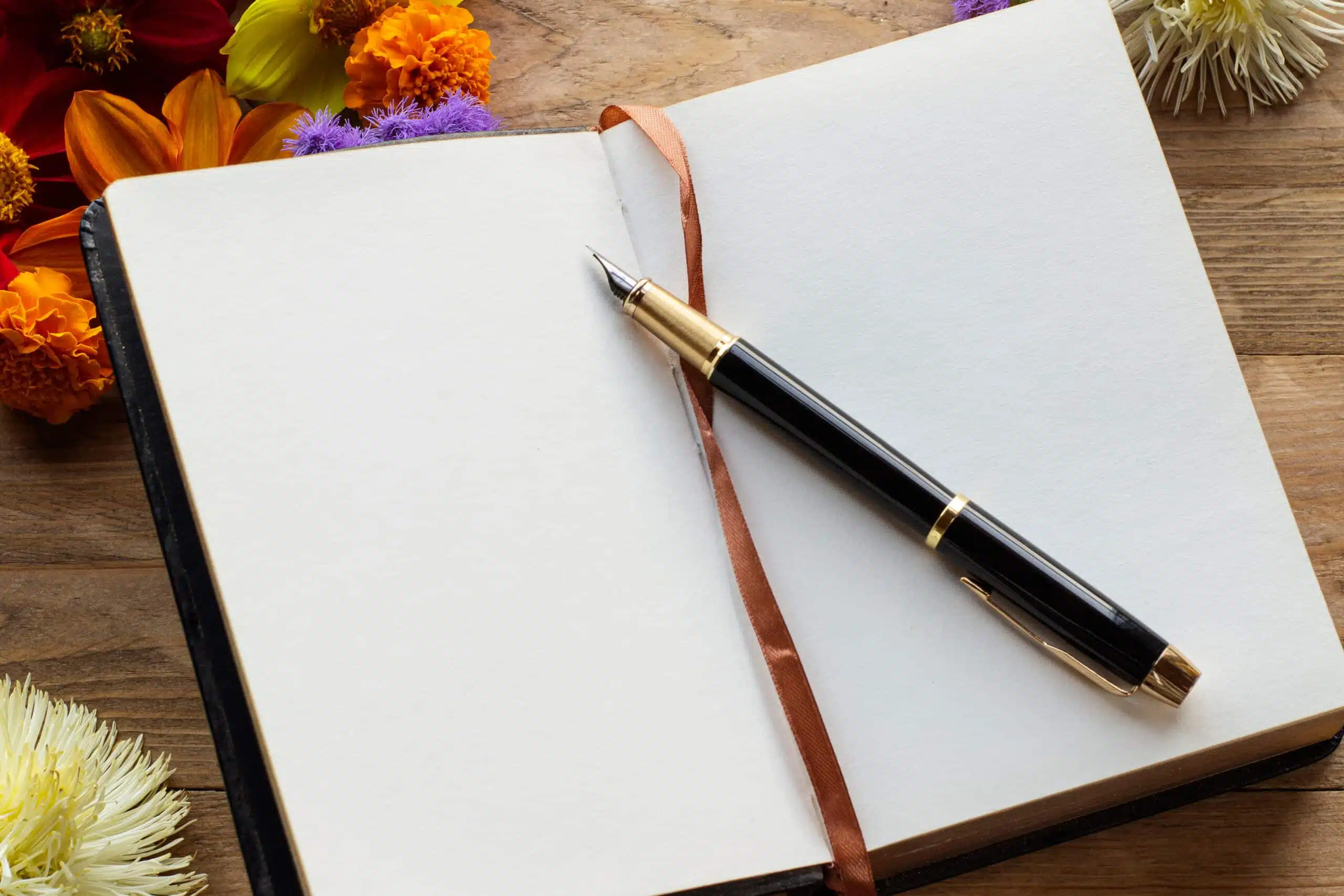 Floral arrangement on a wooden background with an open notebook and fountain pen.