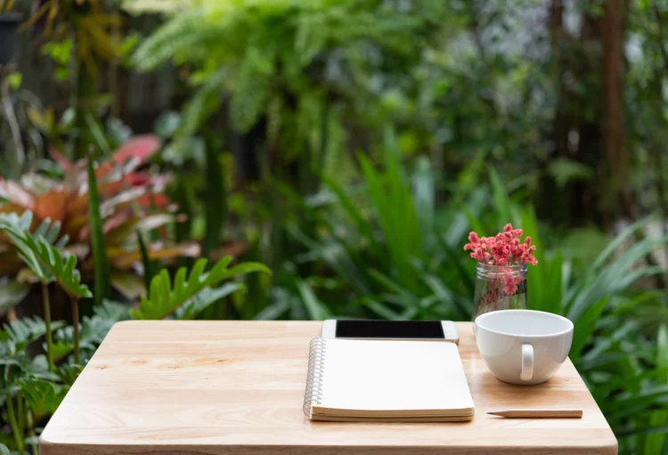wooden desk outdoors with notebook,pencil, and white coffee cup