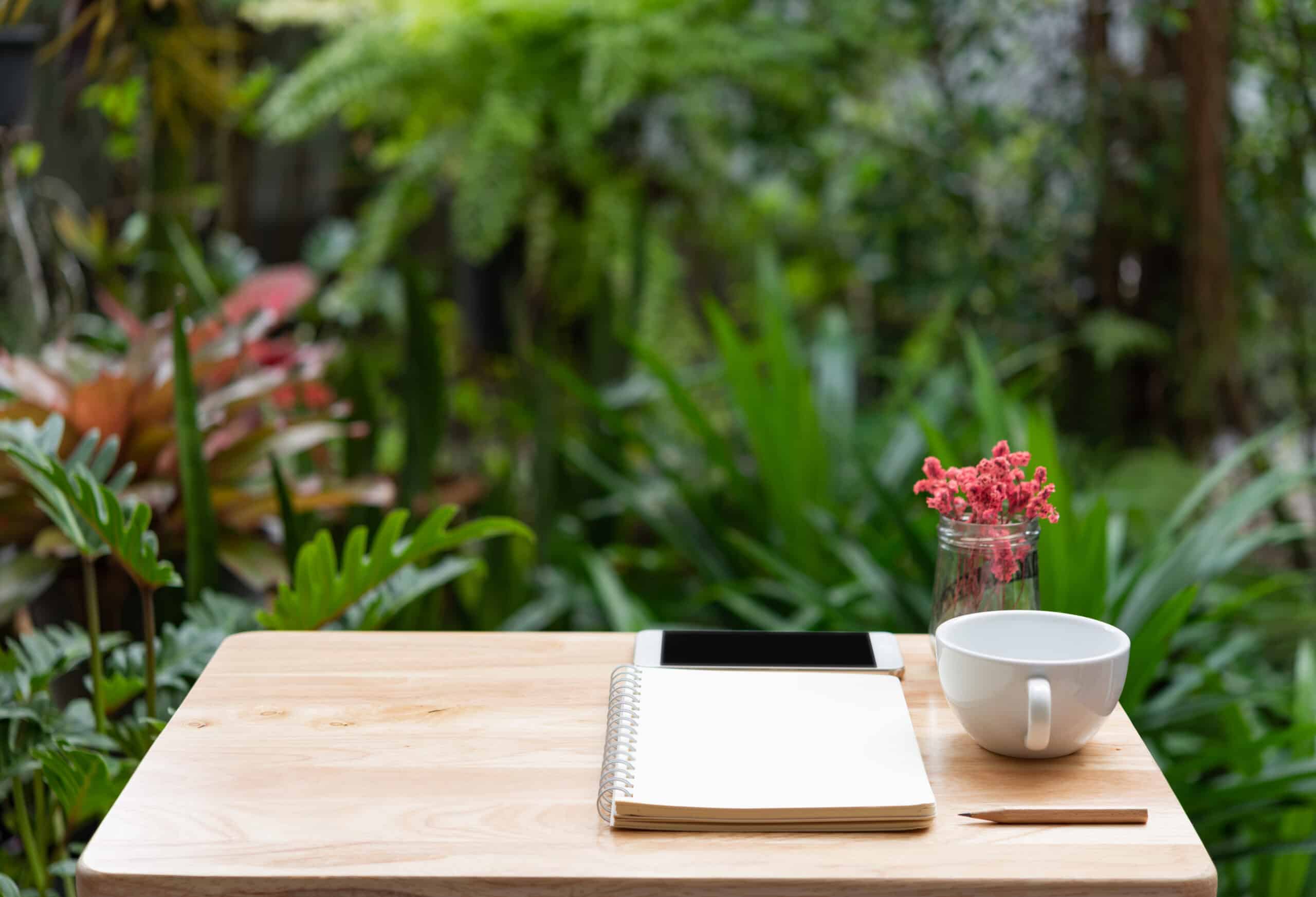 wooden desk outdoors with notebook,pencil, and white coffee cup