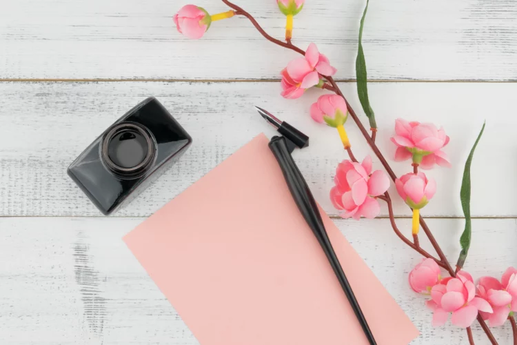 pink paper, pen, inkwell and blooms on a wooden rustic desktop