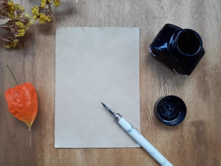 Sheet of paper, white vintage pen, and inkwell on wooden table