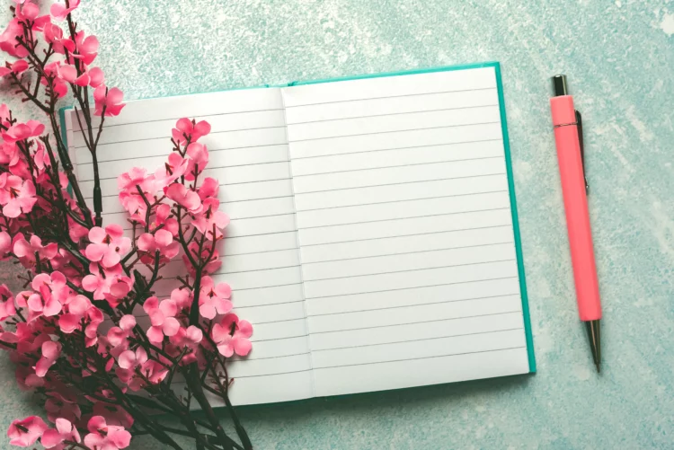 Open empty journal with pink blossoms and pink pen.
