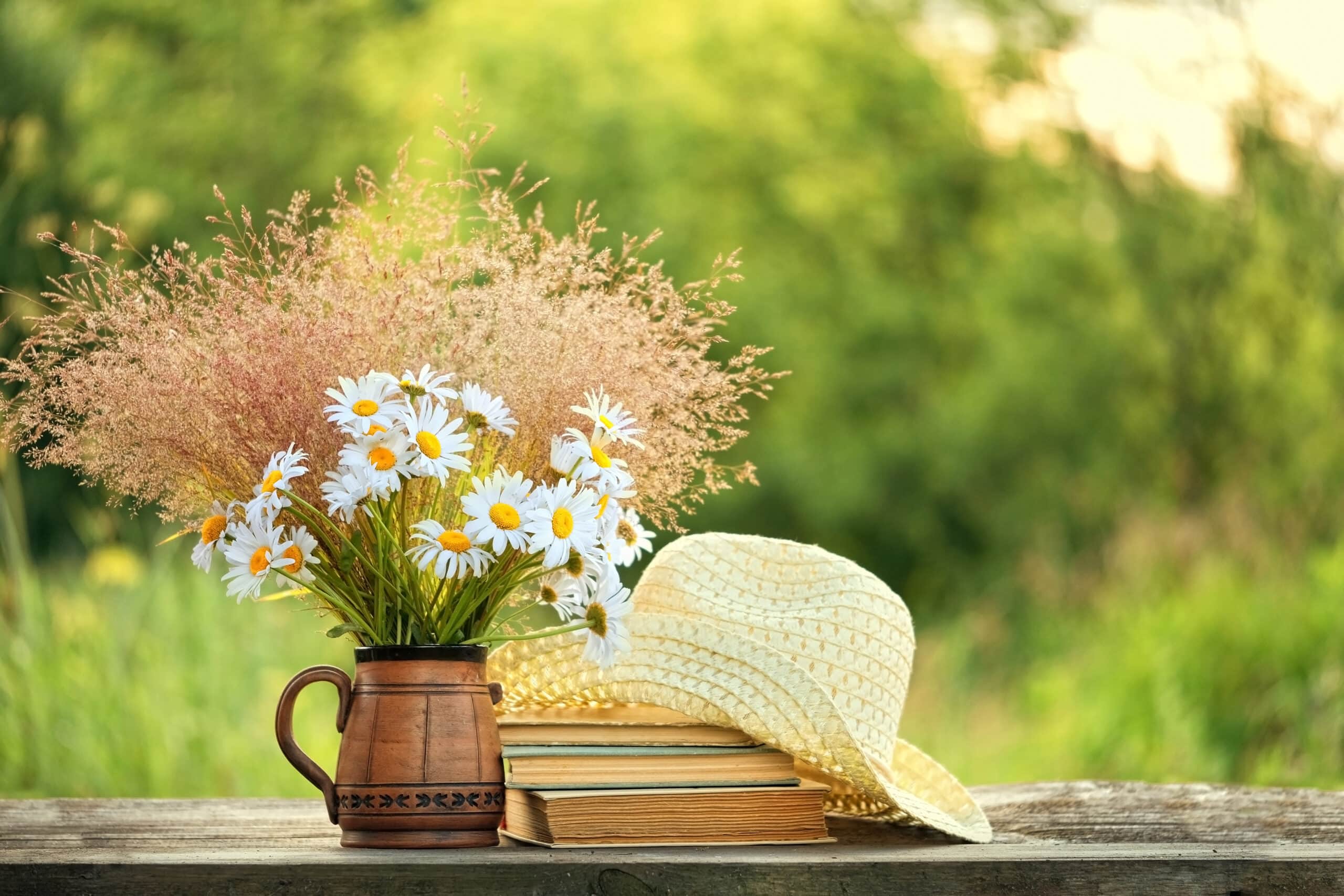 Chamomile flowers, book and summer hat on table in sunny garden.
