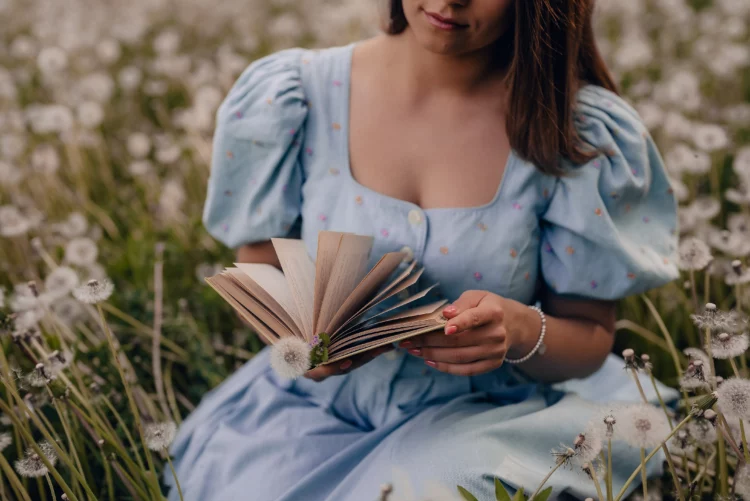 Lady in vintage dress reading interesting book while sitting on nature. 