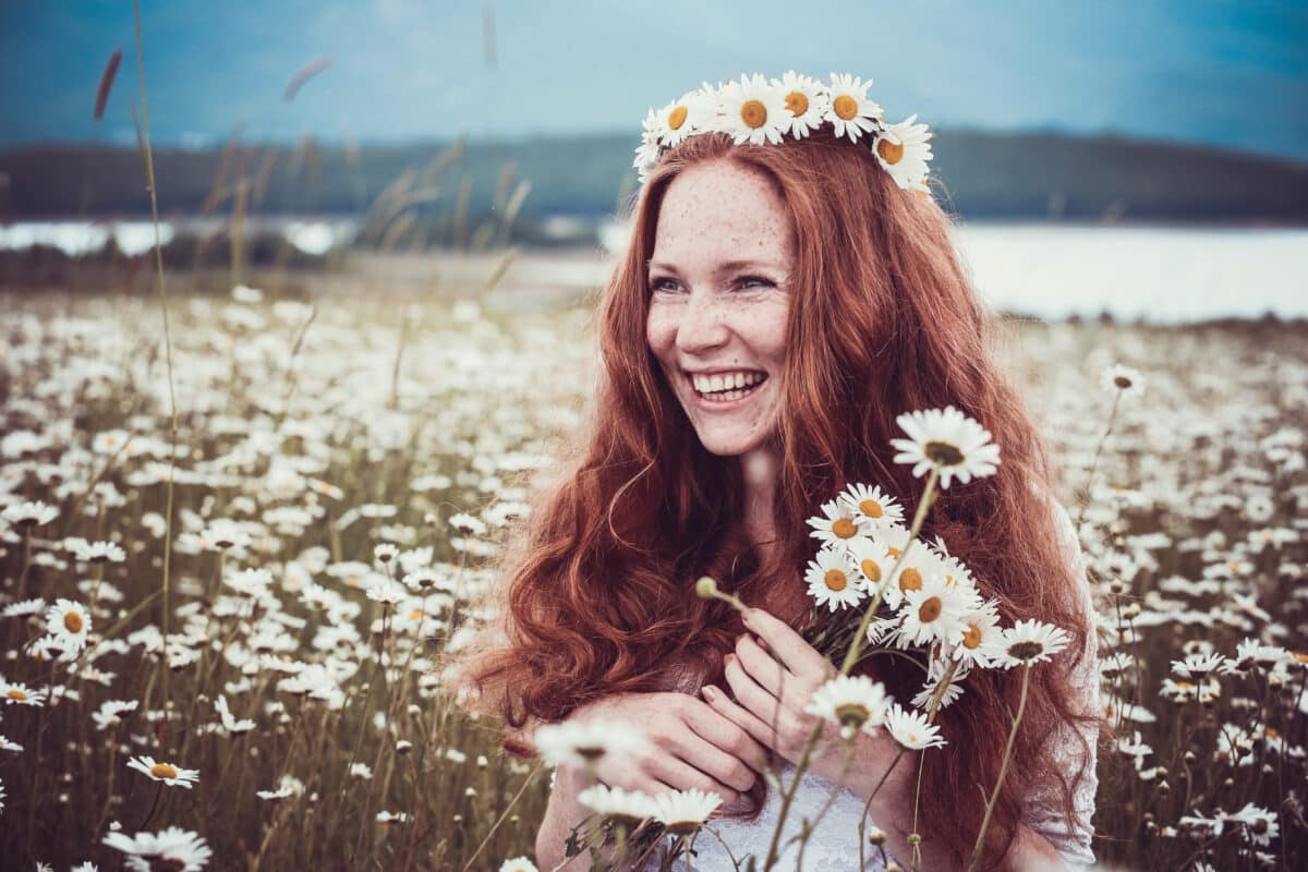 a happy red haired woman having fun in the chamomile field
