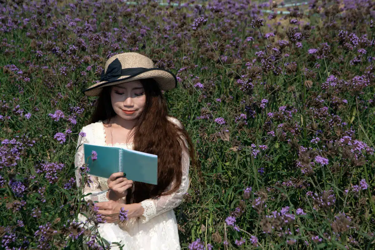 Asian pretty woman  sitting in the flower verbina bonariensis garden and reading a book in different gestures Happily.