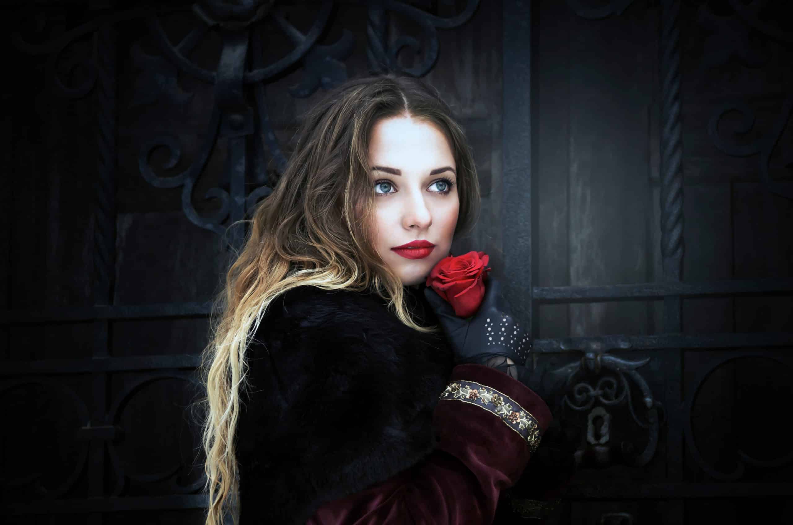 Beautiful long-haired girl holding red rose near the door to the castle.
